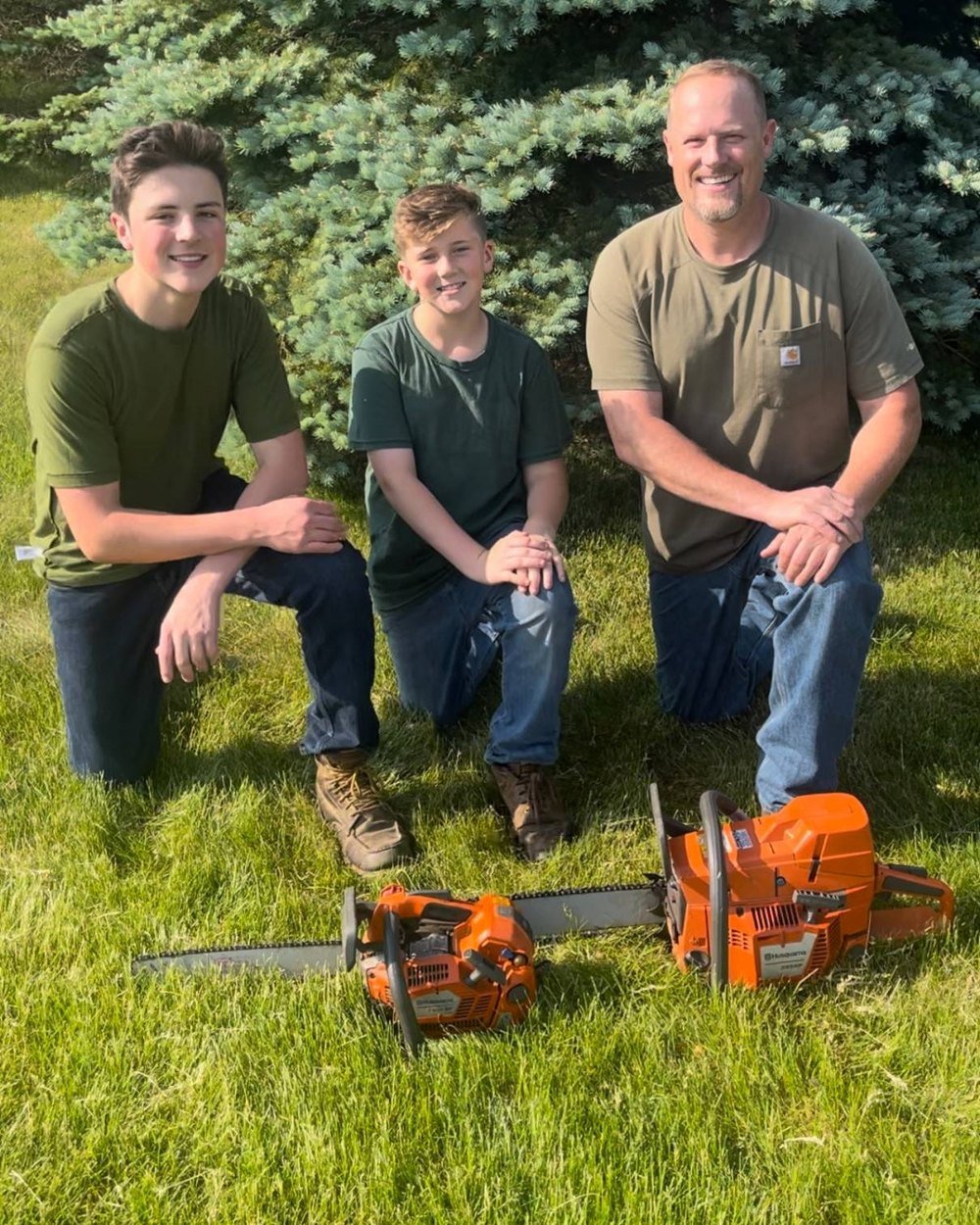 Nathan and his two grown sons kneeling beside their Husqvarna chainsaws