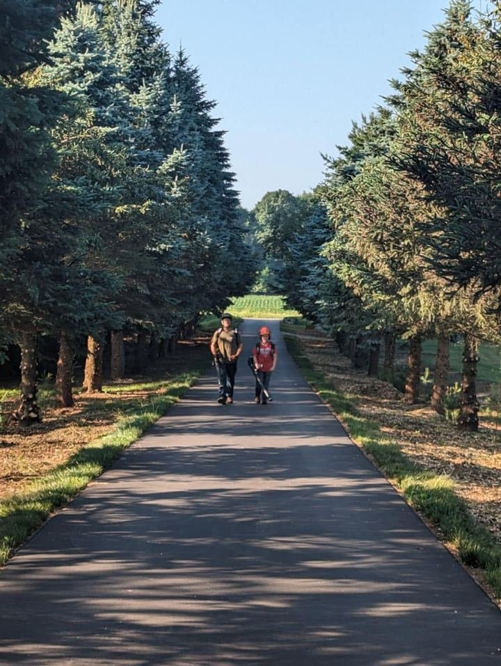 Father and son walking a tree-lined driveway carrying leaf blowers